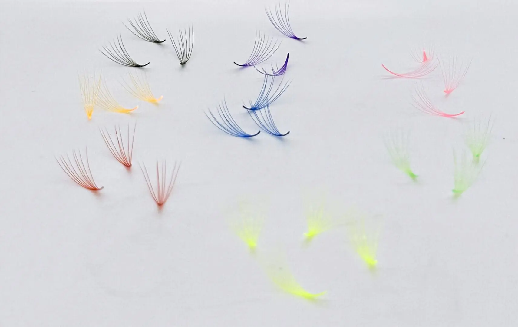 A group of different colored eyelashes on top of white paper.