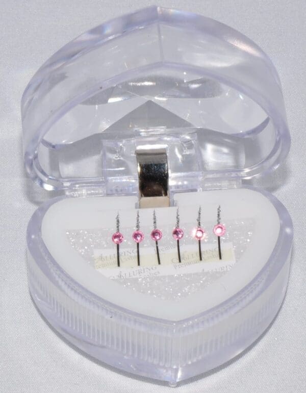 A heart shaped box with six different needles in it.